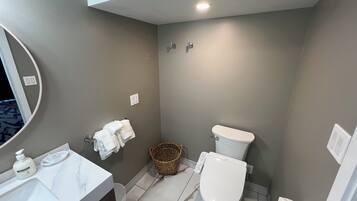Een badkamer met een wit wastafel, toilet, spiegel en mand.