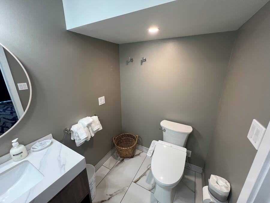 Un baño con lavamanos blanco, inodoro, espejo y cesta.