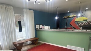 A hotel reception area with a counter, a bench, a red rug, and a window with curtains.