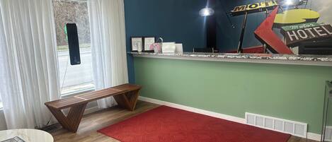 A hotel reception area with a counter, a bench, a red rug, and a window with curtains.