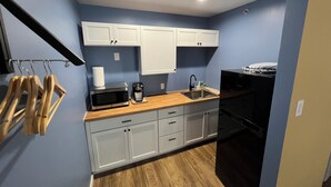 A compact kitchen with white cabinets, a microwave, a coffee maker, and a sink. - Lighthouse Inn & Suites (Hannibal)