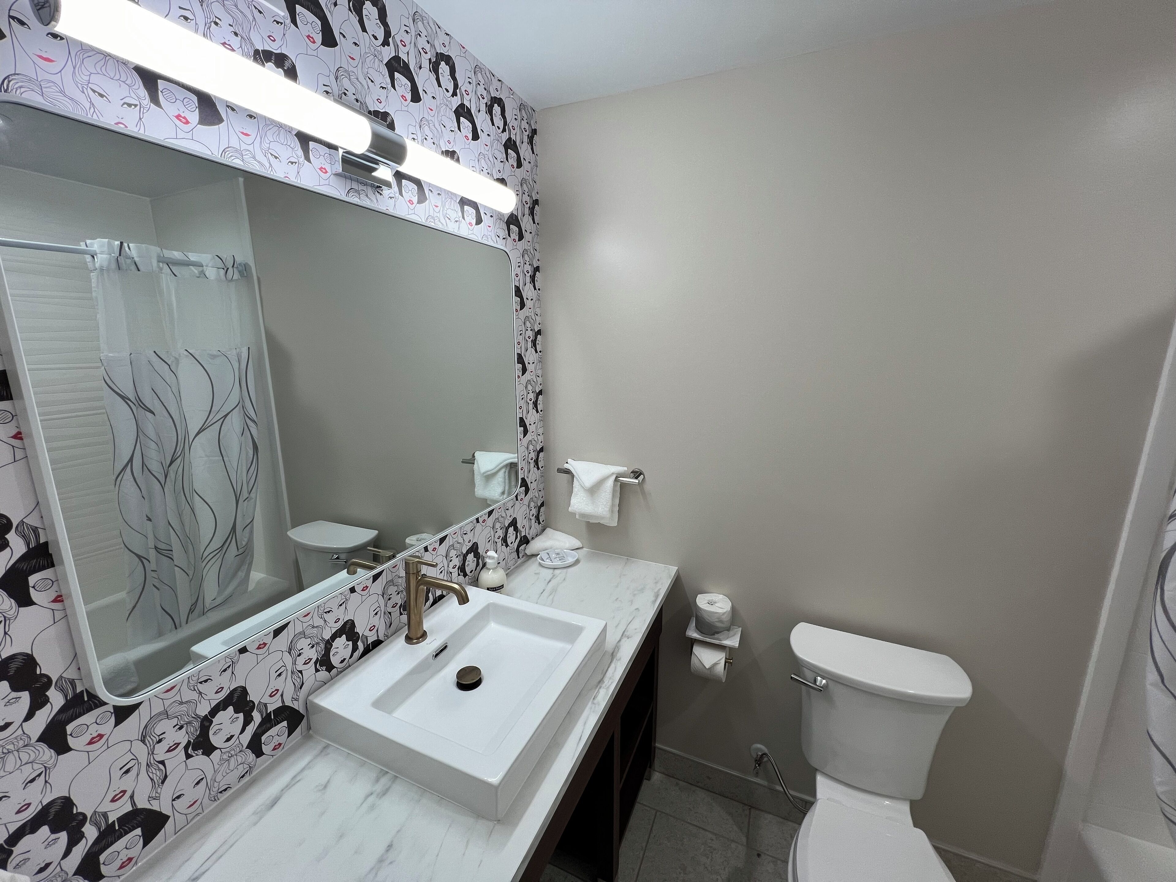 A bathroom with a white sink, a mirror, a toilet, and a shower curtain with a leaf pattern.