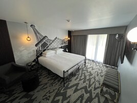Quarto de hotel moderno com uma cama grande, uma obra de arte original na parede, um banco e um tapete estampado.