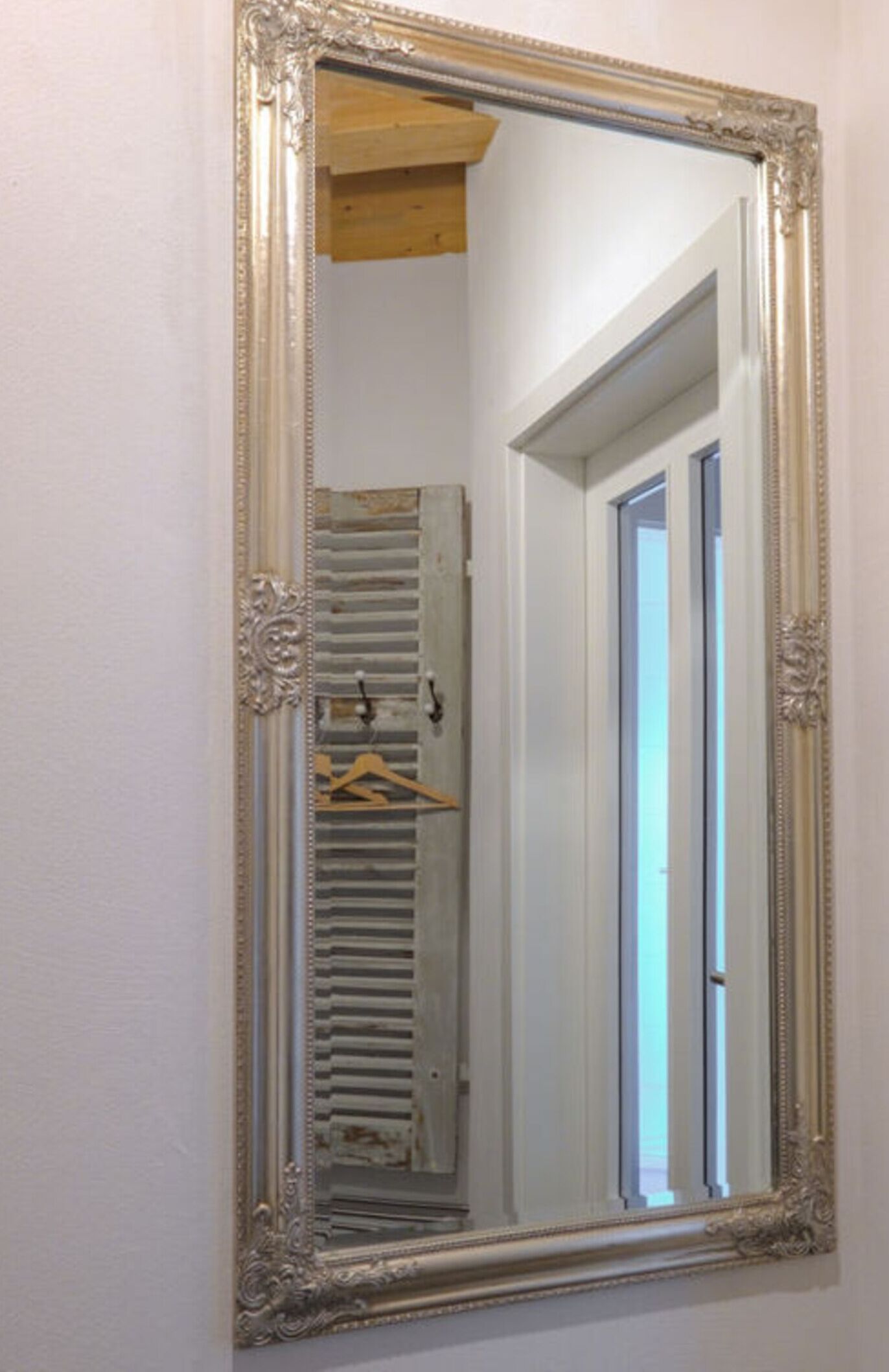 A mirror with an ornate frame reflecting a hallway with a wooden door and a radiator.