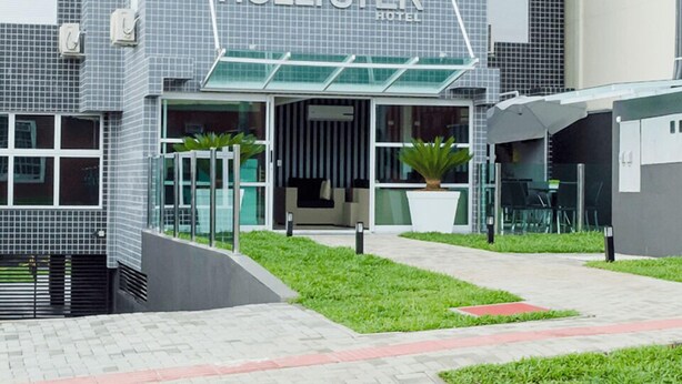 A modern hotel with a tiled facade, a glass entrance, and a green lawn area. - HOLLYSTER HOTEL (Curitiba)