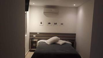 Ein Schlafzimmer mit einem Bett, einem Nachttisch, einem an der Wand befestigten Fernseher und einer Deckenleuchte.