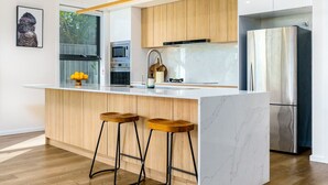 Una cocina moderna con armarios de madera, encimera de mármol, refrigerador de acero inoxidable y dos taburetes de bar.