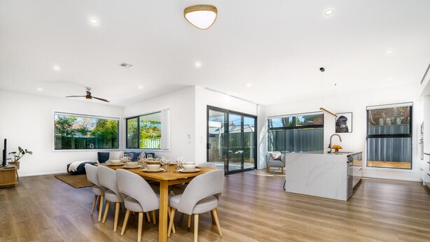 Un comedor espacioso con una mesa y sillas de madera, ventanas amplias y una cocina moderna al fondo.