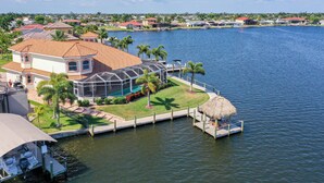 A large house with a swimming pool, a dock, and a thatched structure by the water. - Your Private Paradise Awaits – Experience Luxury at villa paradise (Cape Coral)