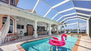 A pool area with a flamingo float, a covered seating area, and a view of the sea. - Your Private Paradise Awaits – Experience Luxury at villa paradise (Cape Coral)