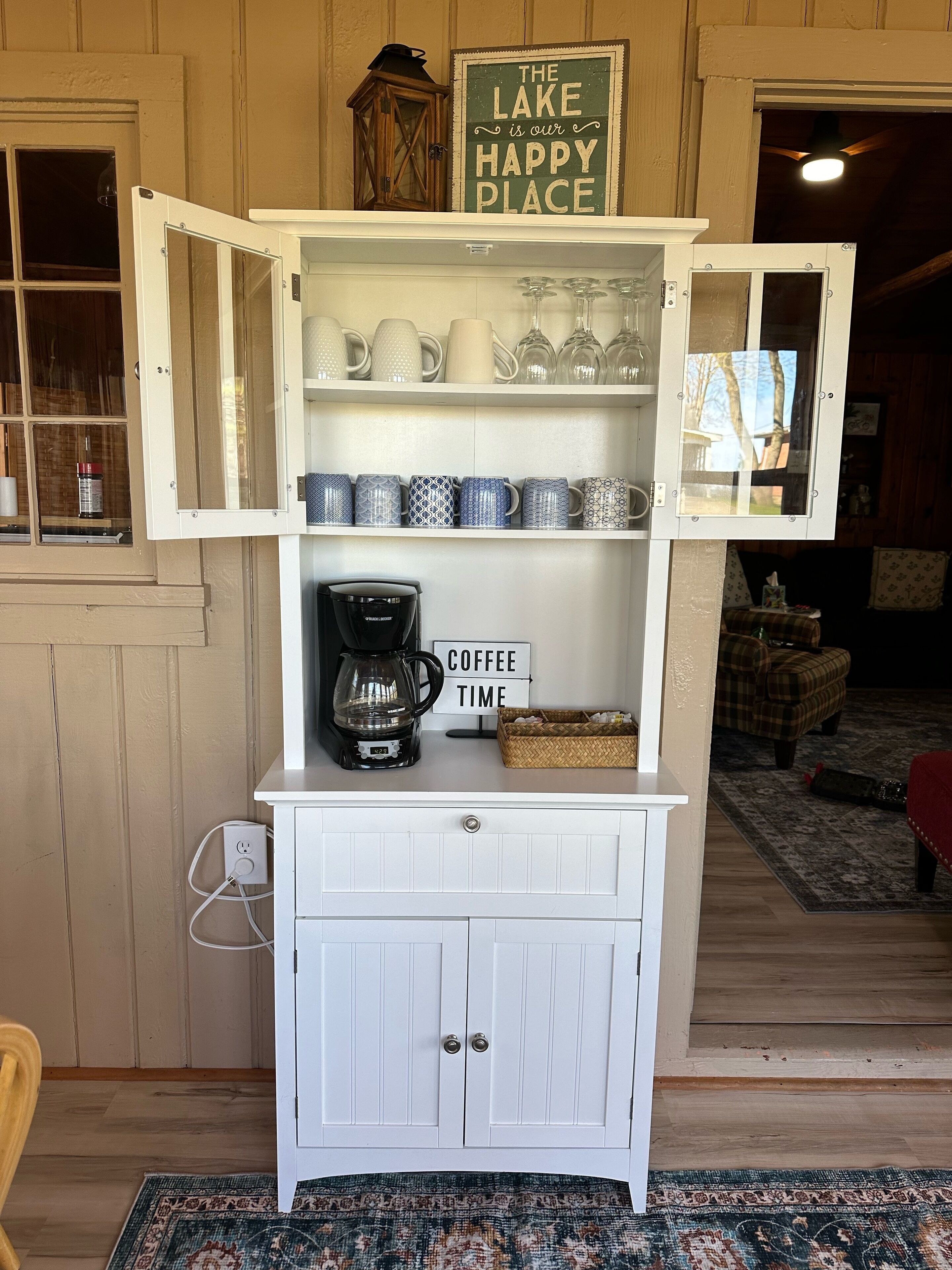 Un mueble blanco con puertas abiertas que muestra tazas, una cafetera y un cartel que dice 'Coffee Time'.