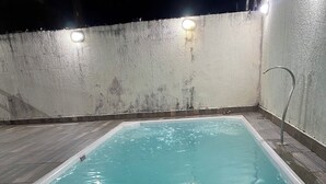 Una piscina rectangular con agua cristalina, rodeada por una terraza de madera y una pared de hormigón.
