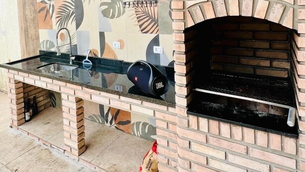 Una cocina con horno de ladrillo empotrado, encimera de vidrio y pared con estampado de hojas tropicales.