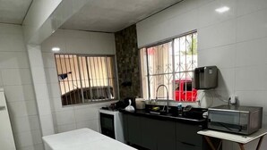 Una cocina compacta con una mesa blanca, bancos, una pequeña encimera y una parrilla portátil.