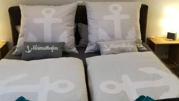 A bed with two pillows featuring anchor designs and the text "Heimathafen". - Charming Apartment in Norden (Norden)