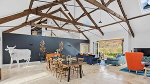 A spacious living area with a high ceiling and exposed beams, a dining table set with chairs, a sofa, and a red armchair. - The Shippon -  Free Parking, Free WiFi, EV Charger, Coffee Machine, Large Garden (Dawlish)