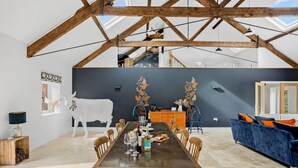 A dining area with a long table, wooden chairs, and a decorative cow sculpture. - The Shippon -  Free Parking, Free WiFi, EV Charger, Coffee Machine, Large Garden (Dawlish)