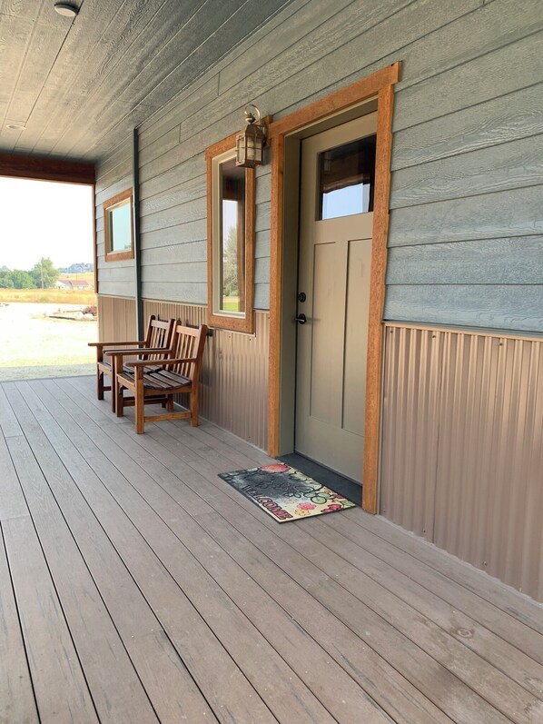 A wooden porch with a bench, a door, and a welcome mat. - The Guest House at Rod and Rifle Ranch (Corvallis)