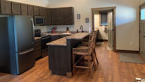 A modern kitchen with dark wooden cabinets, a stainless steel refrigerator, a microwave, and a granite countertop. - The Guest House at Rod and Rifle Ranch (Corvallis)