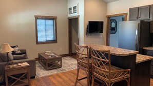 A modern kitchen with a bar area, wooden flooring, and a flat-screen TV mounted above the counter. - The Guest House at Rod and Rifle Ranch (Corvallis)