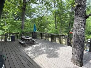 Een houten terras met picknicktafels en een vuilnisbak, omringd door bomen.