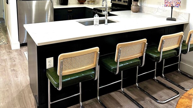 A modern kitchen with white cabinets, stainless steel appliances, a central island with bar stools, and pendant lighting. - The Vault - Perfect Location! (Oxford)