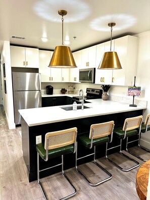 A modern kitchen with white cabinets, stainless steel appliances, a central island with bar stools, and pendant lighting.