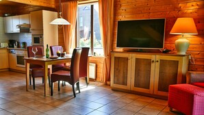A cozy cabin-style room with a dining table, chairs, a television, and a red ottoman. - Find Your Holiday Home in the Harz Mountains (Oberharz am Brocken)