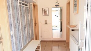 A narrow hallway with a wooden wall, a white bench, a door leading to a room, and a small table with a white cabinet. - Muschelhus Comfortable Holiday Residence (Hohwacht)