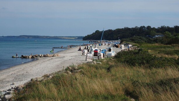 A beach with a pier extending into the water, surrounded by rocks and vegetation. - Muschelhus Comfortable Holiday Residence (Hohwacht)