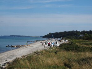 A beach with a pier extending into the water, surrounded by rocks and vegetation. - Muschelhus Comfortable Holiday Residence (Hohwacht)