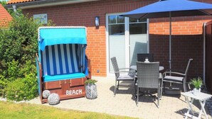 A patio area with a beach chair, wicker chairs, a table, and a blue umbrella. - Muschelhus Comfortable Holiday Residence (Hohwacht)