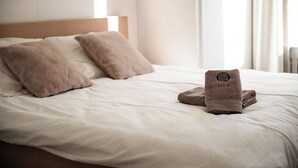 Un lit bien fait, avec deux oreillers et une serviette pliée ornée d’un logo.