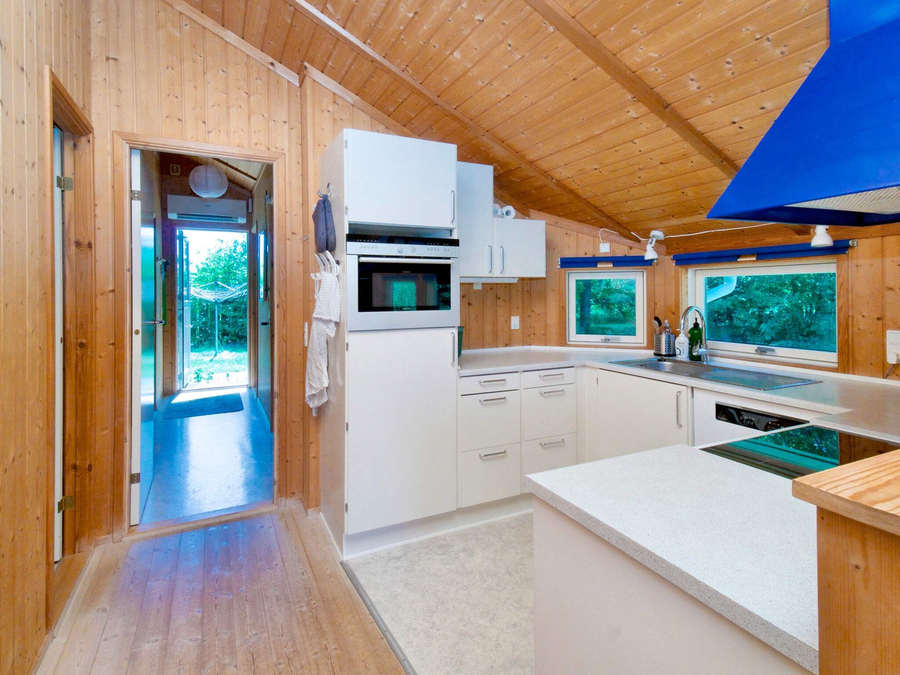 Una cocina moderna con paredes de madera, horno empotrado y ventana con vistas a la vegetación.