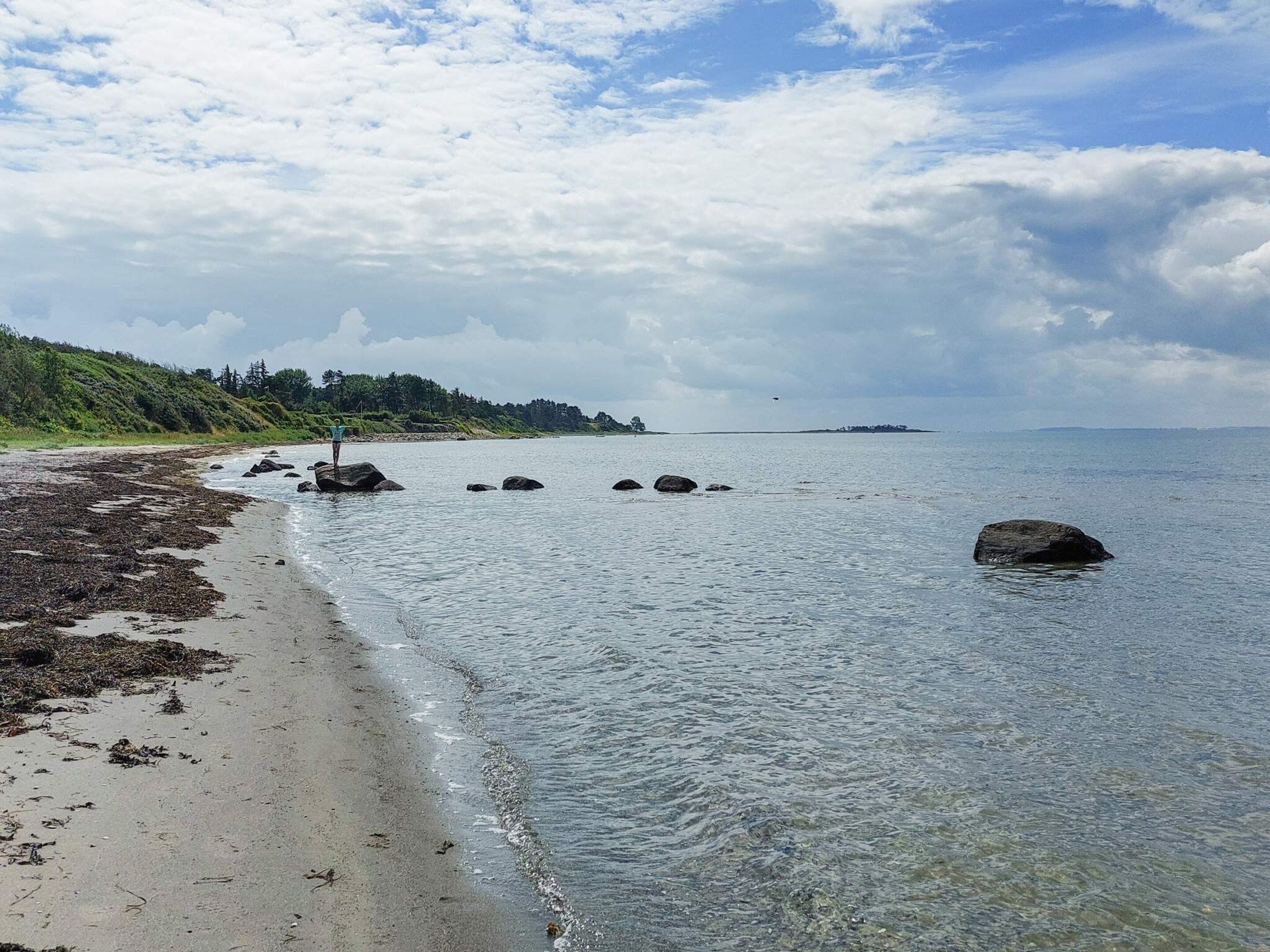 Una playa con agua cristalina, rocas y una isla a lo lejos.