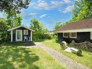 Une petite cabane avec un porche, un bâtiment plus grand avec un toit en tuiles, et un chemin de gravier qui les relie.