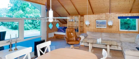 A cozy cabin interior with a dining table, chairs, a sofa, and a bed.