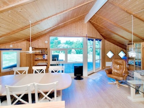 Spazioso loft con soffitto alto, pareti in legno, zona pranzo con mobili bianchi e ampie finestre con vista sull'esterno.