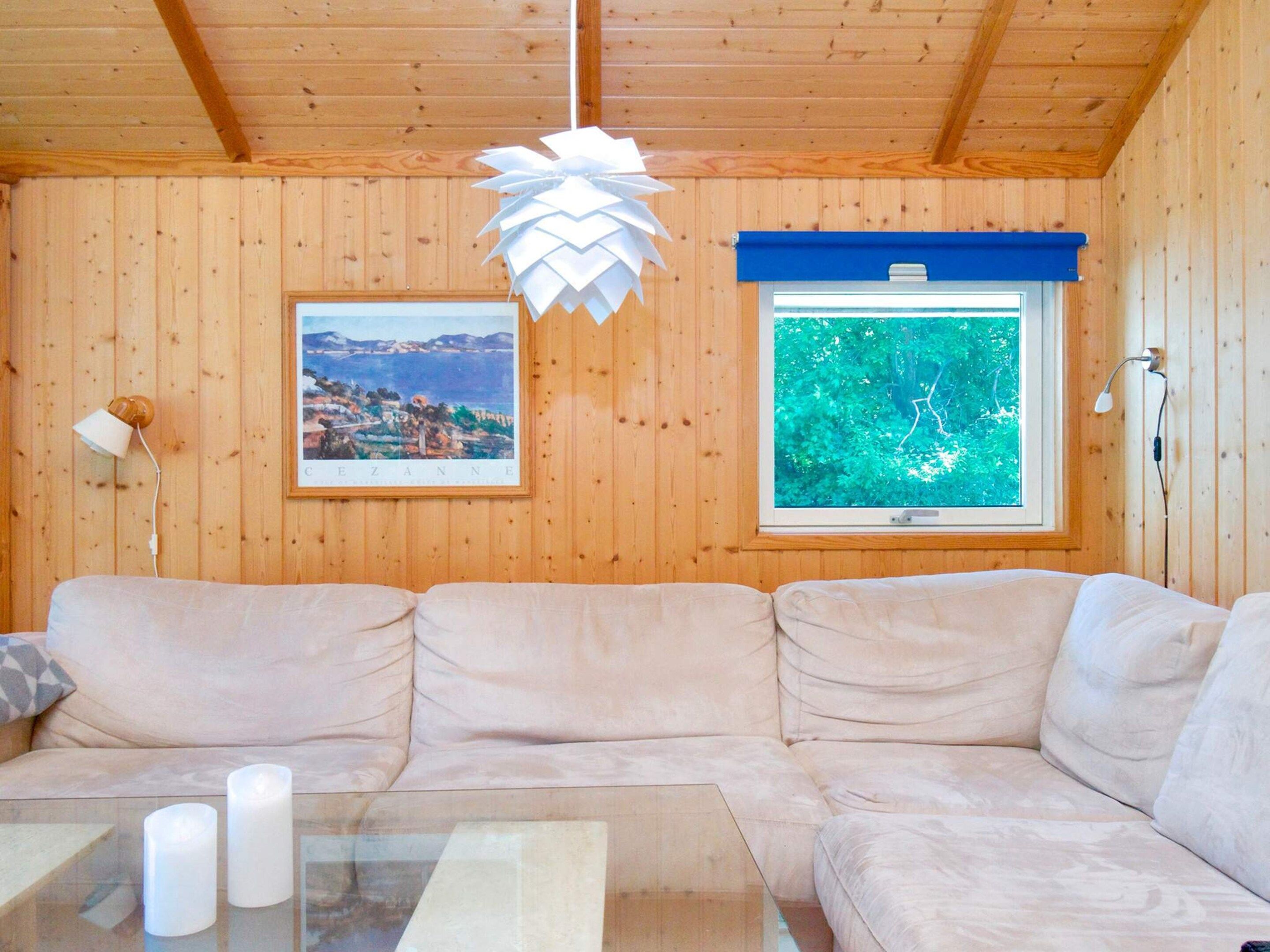 A wooden-paneled room with a beige sofa, a glass coffee table with candles, a framed picture, and a window with a blue blind.