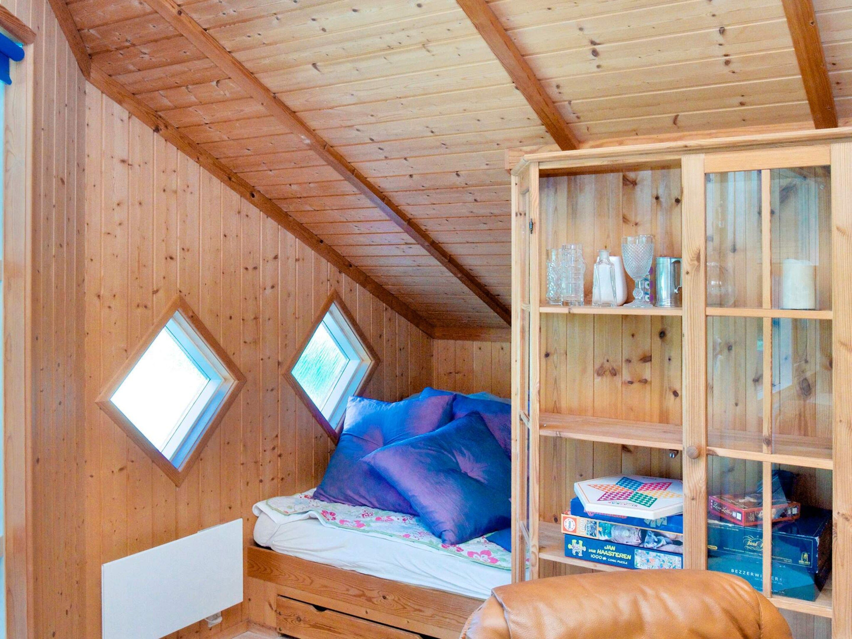 A wooden cabin room with a bed, two skylights, and a cabinet with various items.