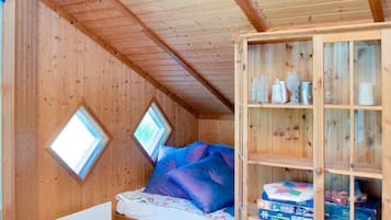 A wooden cabin room with a bed, two skylights, and a cabinet with various items.