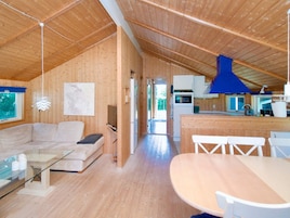 Un interior de madera con un sofá, una mesa de vidrio, una zona de cocina y una mesa de comedor.
