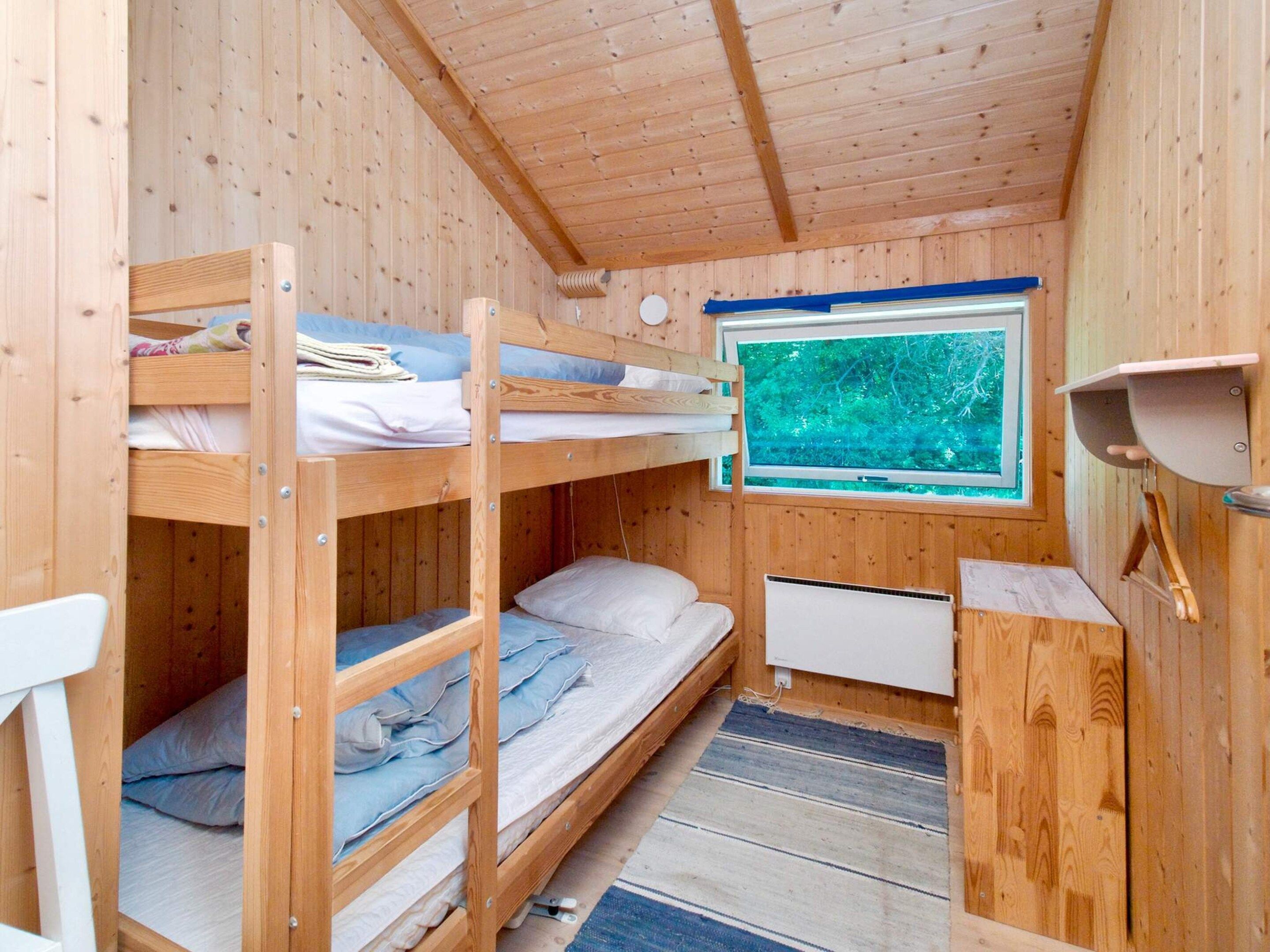 A wooden cabin room with bunk beds, a window with a view of trees, and a small kitchenette area.