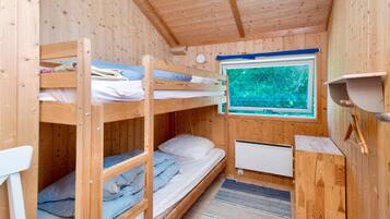 A wooden cabin room with bunk beds, a window with a view of trees, and a small kitchenette area.
