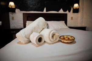 Una cama bien hecha con una toalla blanca enrollada, un rollo de papel higiénico y una cesta de bombones.