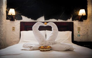 Una habitación de hotel con una cama, dos lámparas de pared y un arreglo decorativo de toallas sobre la cama.