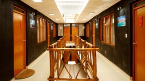 A hotel corridor with wooden doors, a central wooden structure, and framed pictures on the walls. - KW HOTEL (Uyuni)
