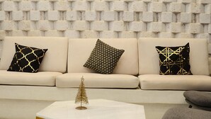 A modern living room with a beige sofa, three patterned pillows, a small decorative tree, and a white coffee table with gold legs. - KW HOTEL (Uyuni)