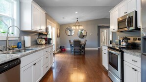 A modern kitchen with white cabinets, stainless steel appliances, and a dining area with a chandelier.