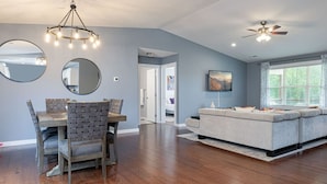 A spacious living room with a dining area, a gray sofa, wooden flooring, and a ceiling fan.